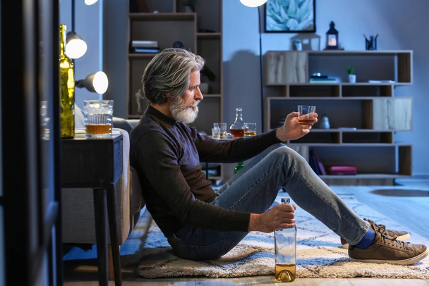 Senior man with glass of drink late in evening at home - Foto, afbeelding