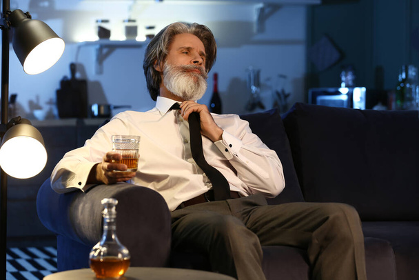 пожилой человек с бокалом напитка поздно вечером дома - Фото, изображение