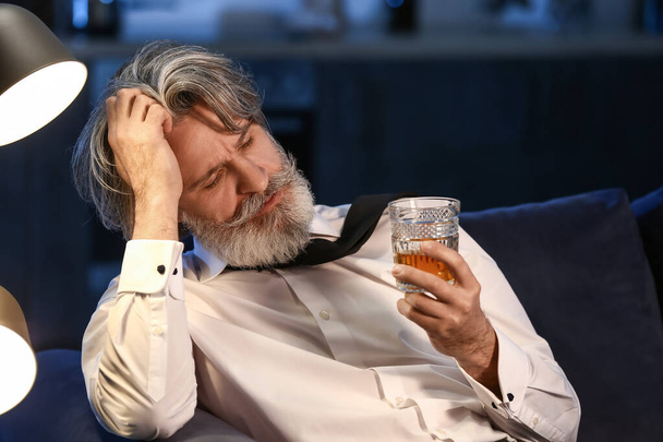 Drunk senior man with glass of whiskey late in evening at home - Fotó, kép
