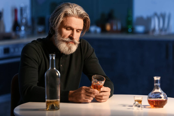 П'яний старший чоловік зі склянкою напою на кухні вночі
 - Фото, зображення