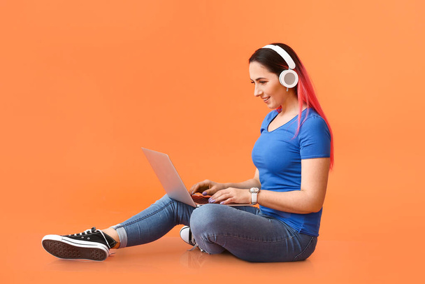 Female programmer with headphones using laptop on color background - 写真・画像