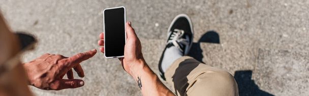 top view of tattooed mature man pointing at smartphone with blank screen, banner - Foto, immagini