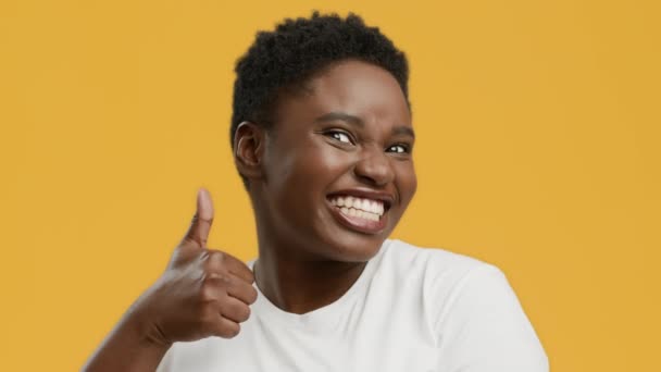 黄色の背景の上に陽気なアフリカ系アメリカ人の太りすぎの女性のジェスチャー親指アップ - 映像、動画