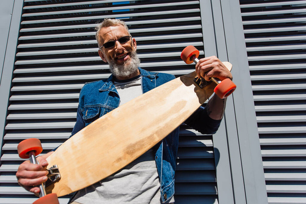 pleased middle aged man in sunglasses holding longboard  - 写真・画像