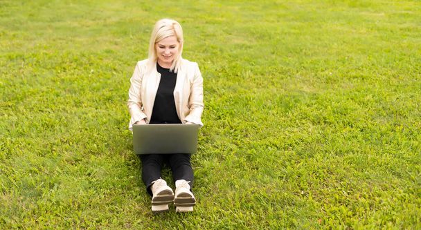 Женщина-копирайтер работает над ноутбуком в парке, смотрит через плечо - Фото, изображение