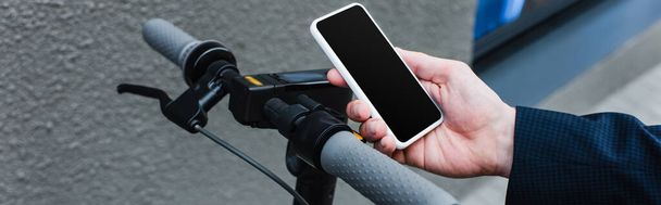 обрізаний вид зрілого бізнесмена, що тримає смартфон з порожнім екраном біля електронного скутера, банер
 - Фото, зображення