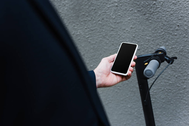 частковий вид зрілого чоловіка, що тримає смартфон з порожнім екраном біля електронного скутера
 - Фото, зображення