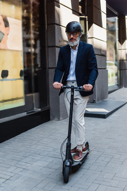 full length of mature businessman in blazer and helmet riding electric scooter  - Φωτογραφία, εικόνα