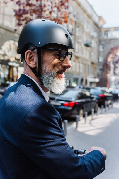 smiling and mature businessman in blazer and helmet riding electric scooter  - Φωτογραφία, εικόνα