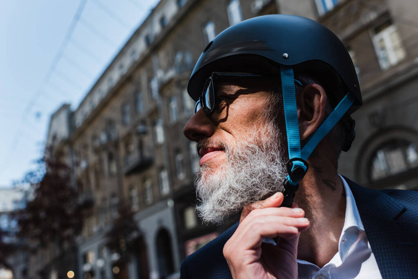 smiling and mature businessman adjusting helmet outside - Foto, Bild