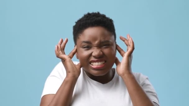 Afrikaanse vrouw met hoofdpijn, het masseren van tempels bedekken oren, blauwe achtergrond - Video