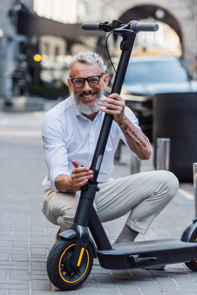 happy mature man adjusting electric scooter on street  - Foto, Imagen