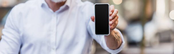 обрізаний вид чоловіка середнього віку, що тримає мобільний телефон з порожнім екраном, банер
 - Фото, зображення
