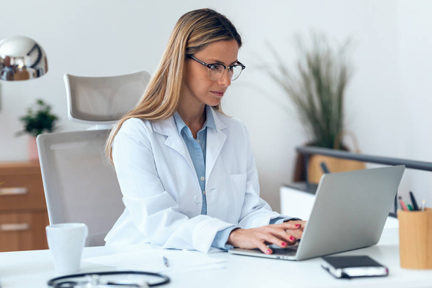 Shot of mature concentrated attractive female doctor working with her computer in the consultation. - Φωτογραφία, εικόνα