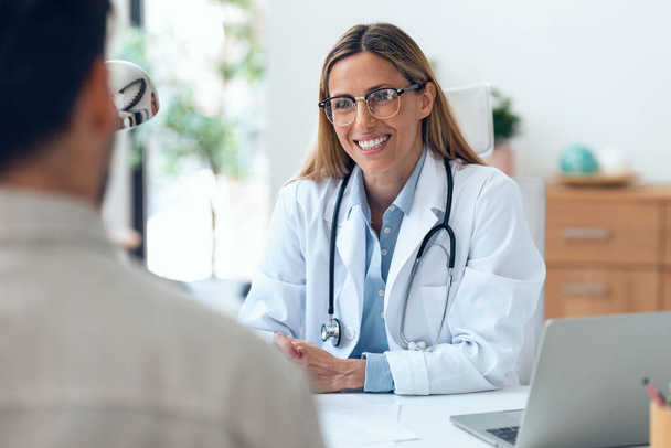 Shot of beautiful mature female doctor talking while explaining medical treatment while prescribing medication to patient in the consultation. - Foto, afbeelding