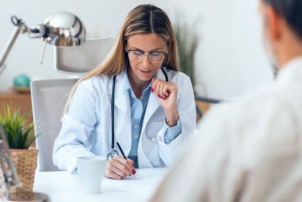Shot of beautiful mature female doctor talking while explaining medical treatment while prescribing medication to patient in the consultation. - Foto, afbeelding