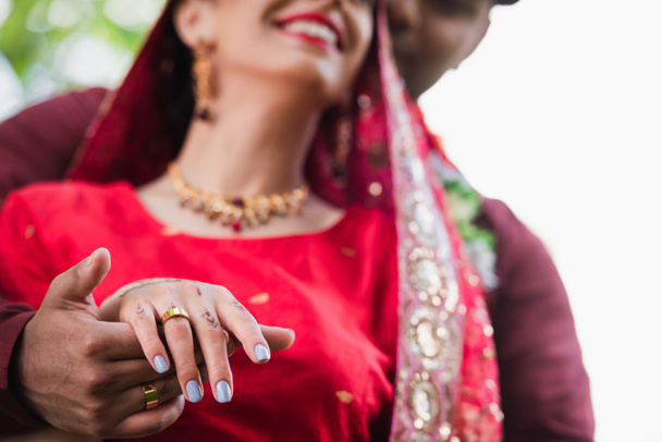 Teilansicht eines glücklichen indischen Mannes, der die Hand der Braut mit dem Ehering am Finger hält - Foto, Bild