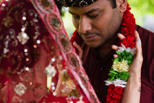Индийская невеста в цветочных гирляндах на женихе снаружи - Фото, изображение