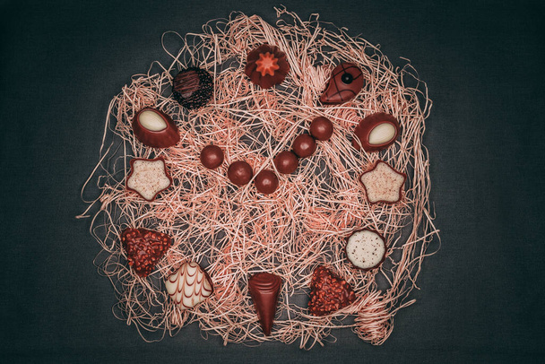 A closeup of chocolate candies placed on straw decoration on the black background. Top view. - Foto, Bild