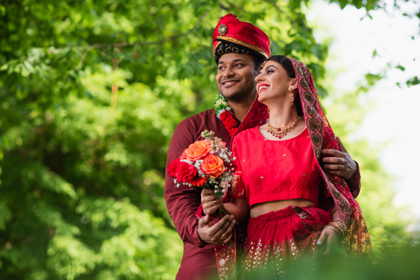 fröhlicher indischer Mann im Turban umarmt Braut in rotem Sari  - Foto, Bild