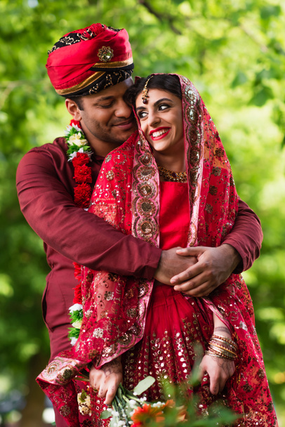 happy indian man in turban hugging bride in red sari  - Foto, afbeelding