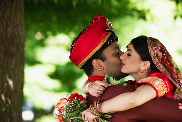 Indian man in turban kissing pretty bride in traditional headscarf  - Фото, зображення