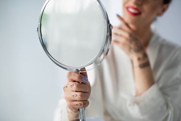 vista cortada de noiva indiana turva e feliz olhando espelho isolado no branco - Foto, Imagem