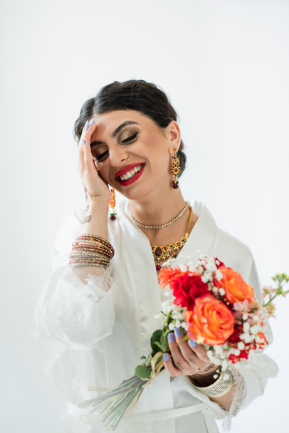 cheerful indian bride with mehndi holding bouquet of flowers on white - Foto, immagini
