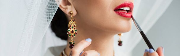 cropped view of indian bride applying lipstick with cosmetic brush on white, banner - Foto, Imagen