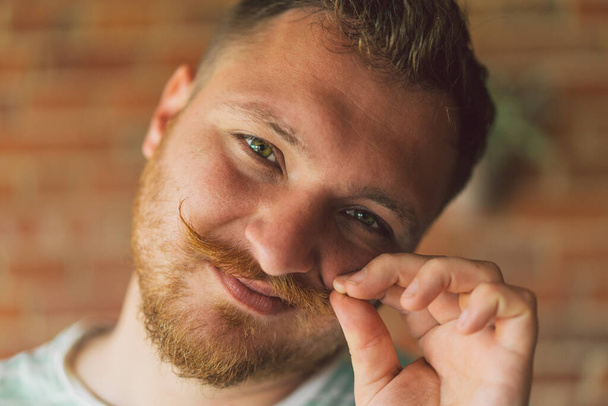 Close up portrait of handsome manly guy with beard and mustache looking in camera and happily smiling - Fotó, kép