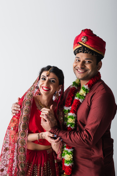 позитивний індійський чоловік і дружина в традиційному одязі тримають руки ізольовані на сірому
 - Фото, зображення