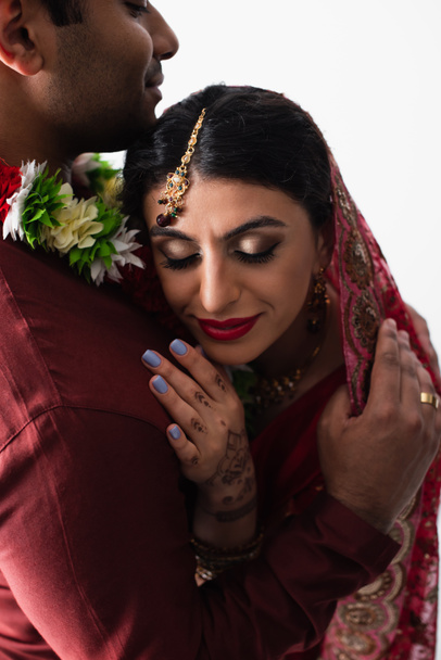 Жених обнимает довольную индийскую невесту в платке, изолированном на белом - Фото, изображение