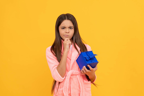 вдумлива дівчина-підліток в домашньому махровому халаті з подарунком або подарунковою коробкою, подарунок
 - Фото, зображення