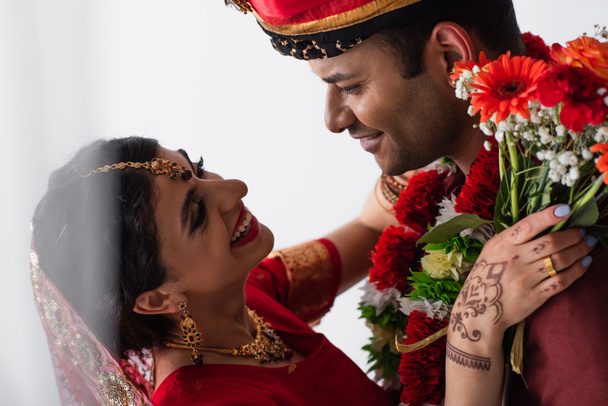 Ευτυχισμένος Ινδιάνος με τουρμπάνι να κοιτάζει την ευτυχισμένη νύφη με τη Μέντι να κρατάει λουλούδια στα λευκά - Φωτογραφία, εικόνα
