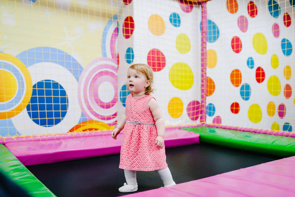 A little baby girl 1-2 years playing and jumping on a trampoline in a children's playroom for her birthday. entertainment centre. - Photo, Image