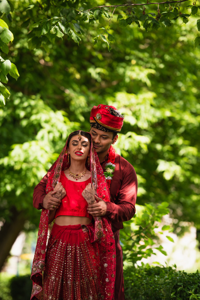 felice uomo indiano in turbante abbracciare la sposa con mehndi in sari e velo  - Foto, immagini