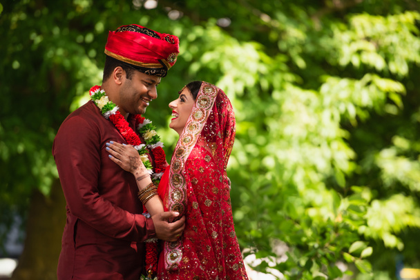 счастливый индийский мужчина в тюрбане обнимает счастливую невесту с mehndi в сари и платке  - Фото, изображение