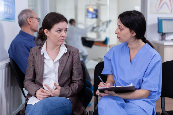 Медсестра делает заметки в блокноте обсуждения с пациентом в стоматологической клинике - Фото, изображение