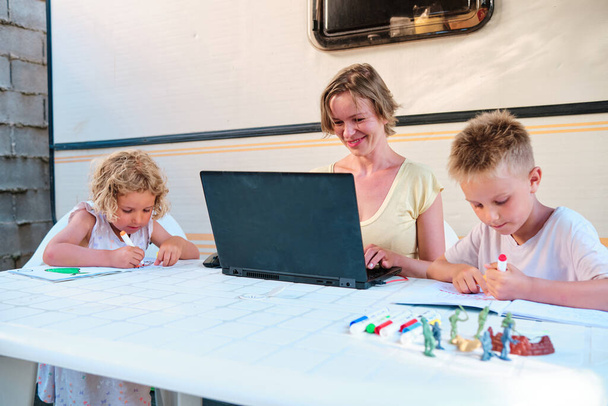 Yazın karavanda bir aile. Anne çalışıyor, çocuklar resim çiziyor ve boş zaman geçiriyor. - Fotoğraf, Görsel