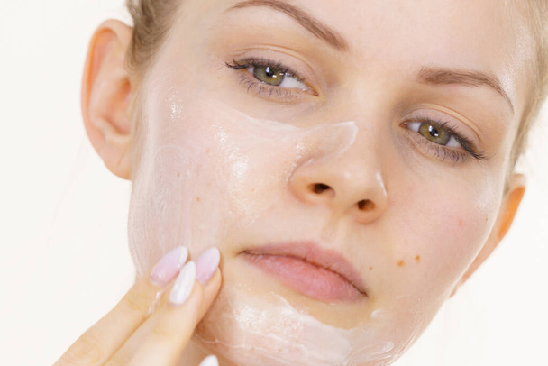 Young woman applying cream cosmetic, mask moisturizing to her face. Beauty treatment. Skincare. - Foto, Imagen
