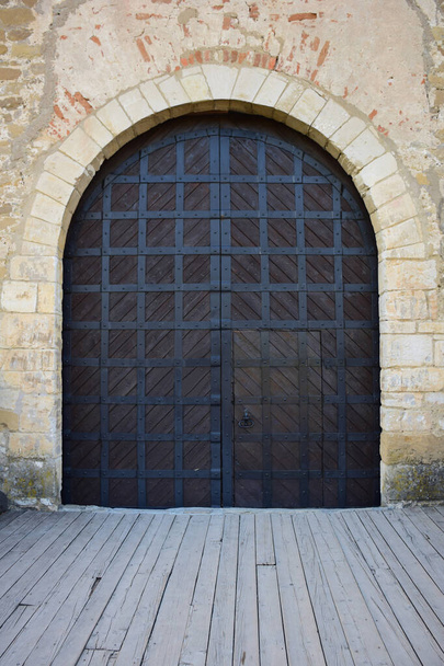 Puertas de madera de un antiguo castillo o fortaleza medieval, cubiertas con tiras de hierro. La puerta tiene un wicket cerrado con un mango - Foto, imagen
