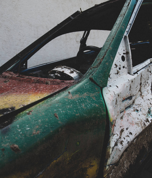 A vertical shot of the broken remains of a car with missing windows and dents all over it - Fotó, kép