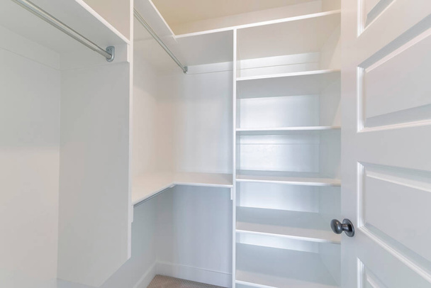 Walk in closet interior con estantes vacíos y varillas vistas desde la puerta abierta - Foto, Imagen