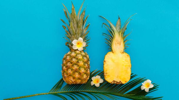 Pineapples whole tropical summer pineapples fruits and sliced pineapple halves with tropical plumeria flowers composition on blue color summer background. Flat lay long web banner - Foto, imagen