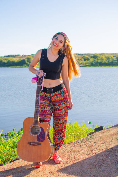 A pretty blonde Argentinian woman with a guitar on her foot posing on the riverside - 写真・画像