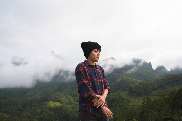 Ασιάτης νεαρός άνδρας με σκωτσέζικο πουκάμισο και μαύρο καπέλο πεζοπορία στην κορυφή του βουνού πάνω από τα σύννεφα και ομίχλη Πεζοπόρος εξωτερική. Επαρχία Doi Luang Chiang Dao Chiangmai, το πρωί. - Φωτογραφία, εικόνα