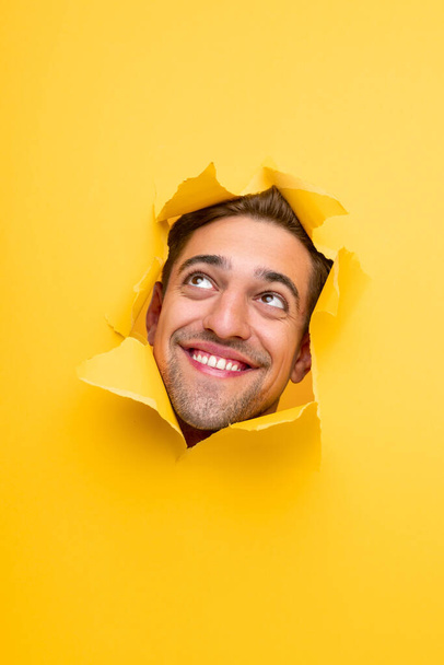 Funny smiling man looking through hole in yellow paper - Fotoğraf, Görsel