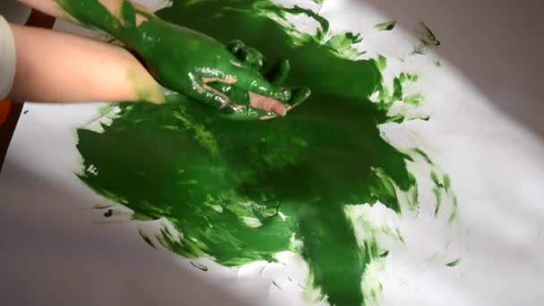 Tyttö sotkee vihreää maalia käsiin ja piirtää paperille - Materiaali, video