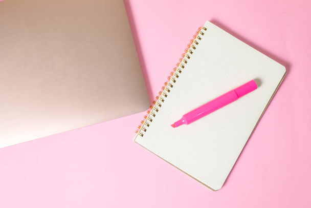 A top view of a marker on an open notebook beside a laptop isolated on a pink surface with copyspace - Foto, Imagem