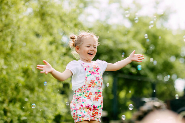 Una chica alegre atrapa burbujas de jabón con las manos y se ríe. Feliz infancia, hora de verano - Foto, imagen